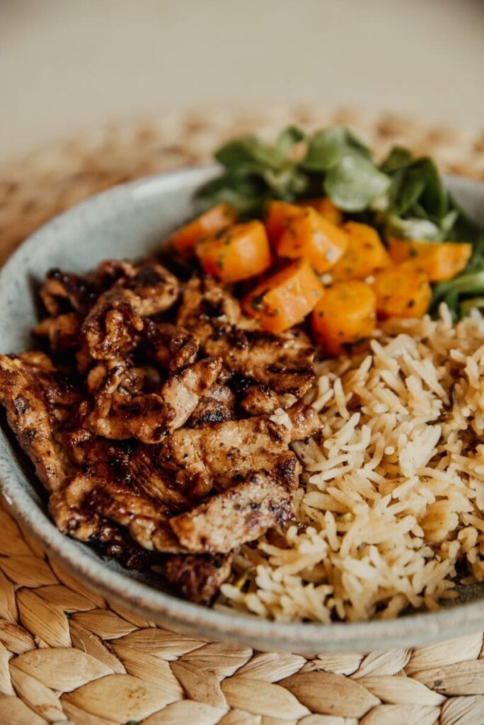 Tasty grilled chicken with rice and colorful vegetables served in a bowl, perfect for a healthy meal.